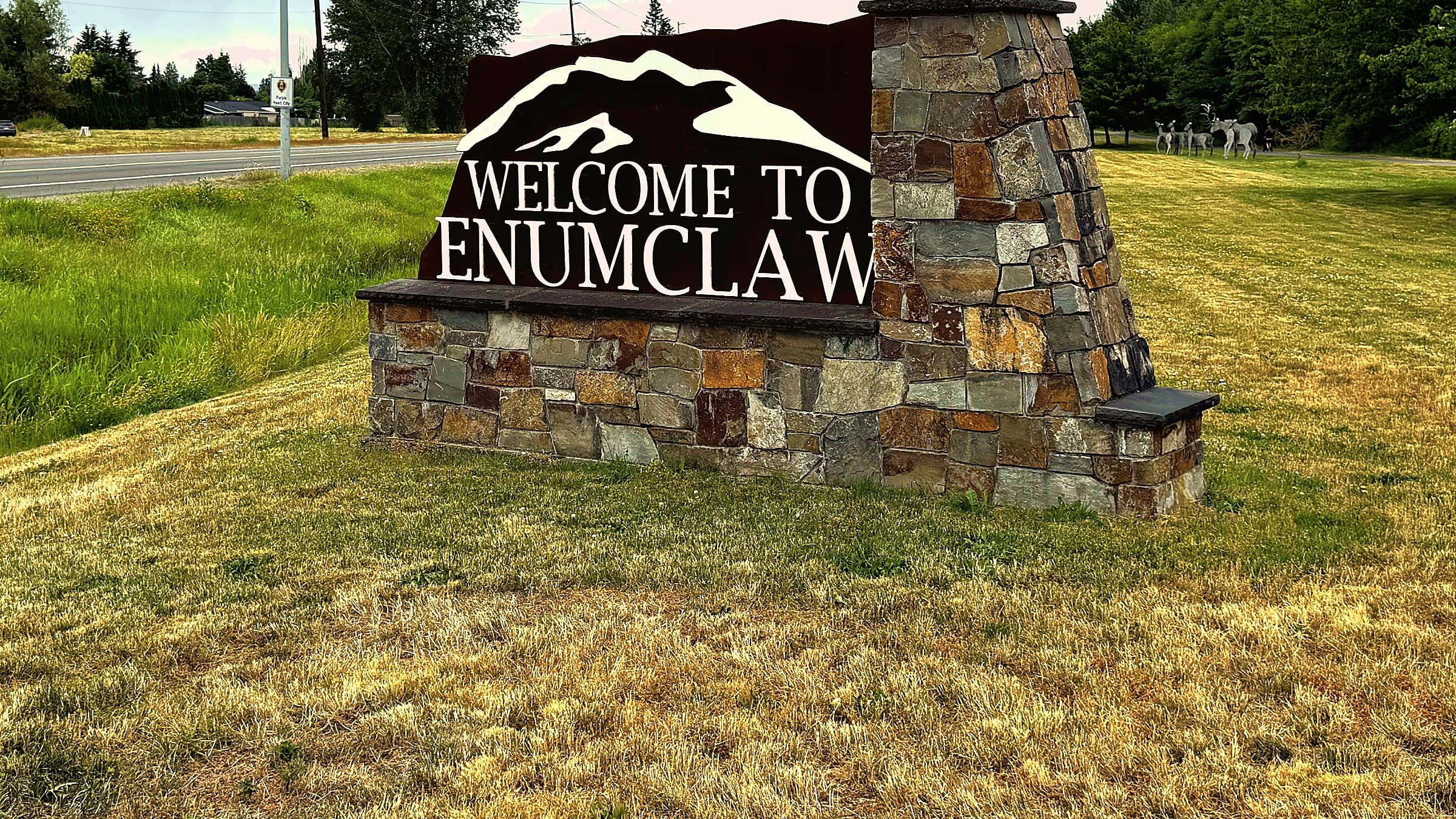 The stone Welcome to Enumclaw sign beside the highway into town, with the foothills behind it