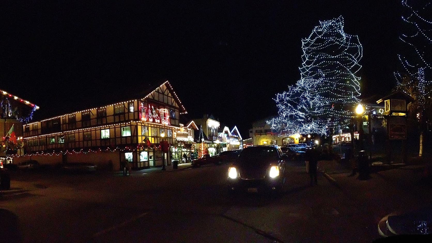 Front Street in Leavenworth, Washington, at night in December 2012, with a half-timbered building outlined in white Christmas lights, lit storefronts down the street and a tall tree wrapped in white lights.