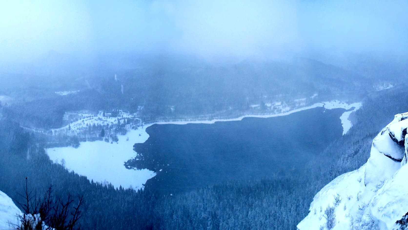 The view from Rattlesnake Ledge in January, with snow-covered rock in the foreground, Rattlesnake Lake below partly frozen and edged with snow, and snowy forest fading into low cloud and mist.