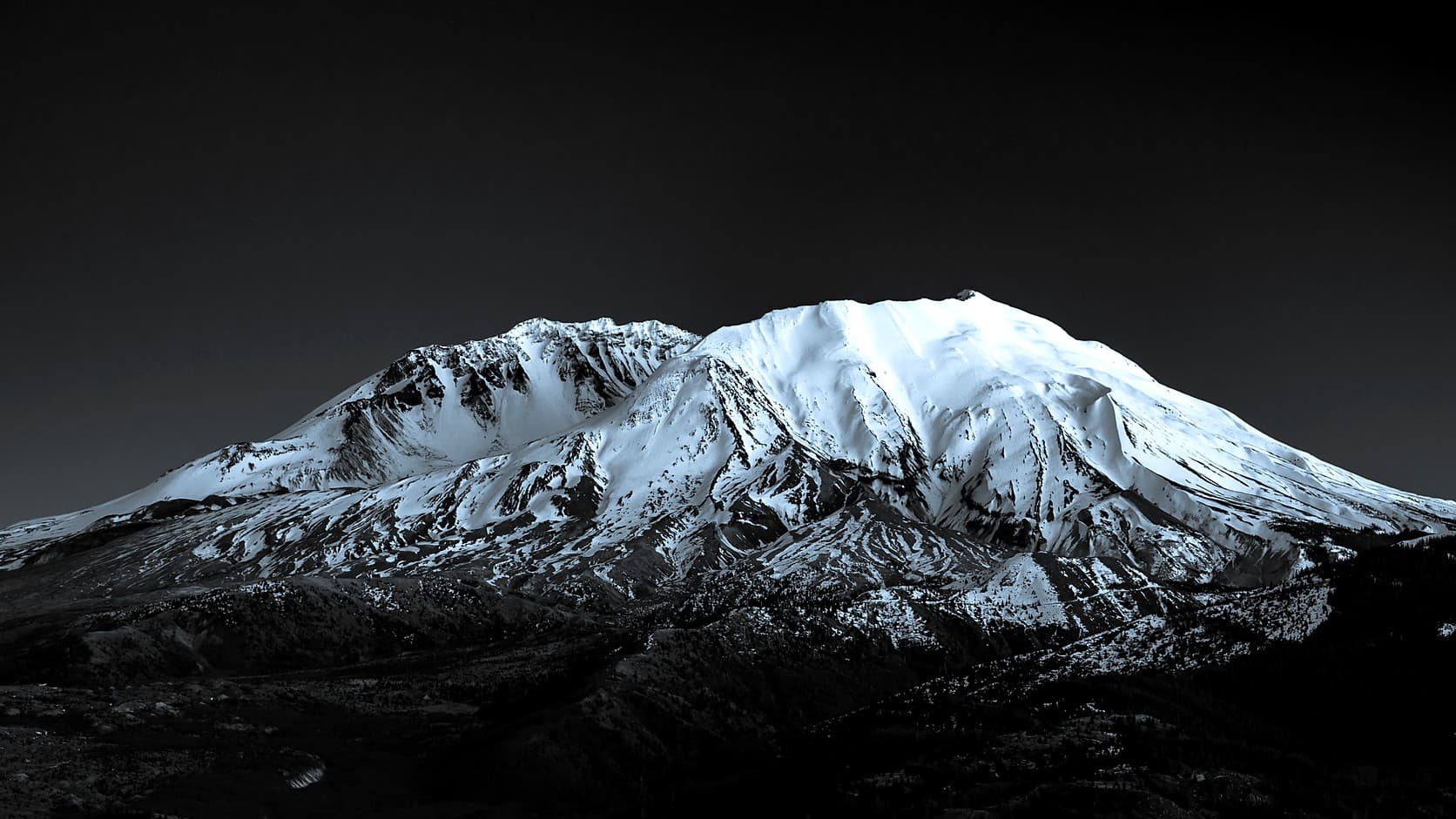 Snow-covered Mount St. Helens against a near-black sky, photographed in monochrome with a cool blue tone.