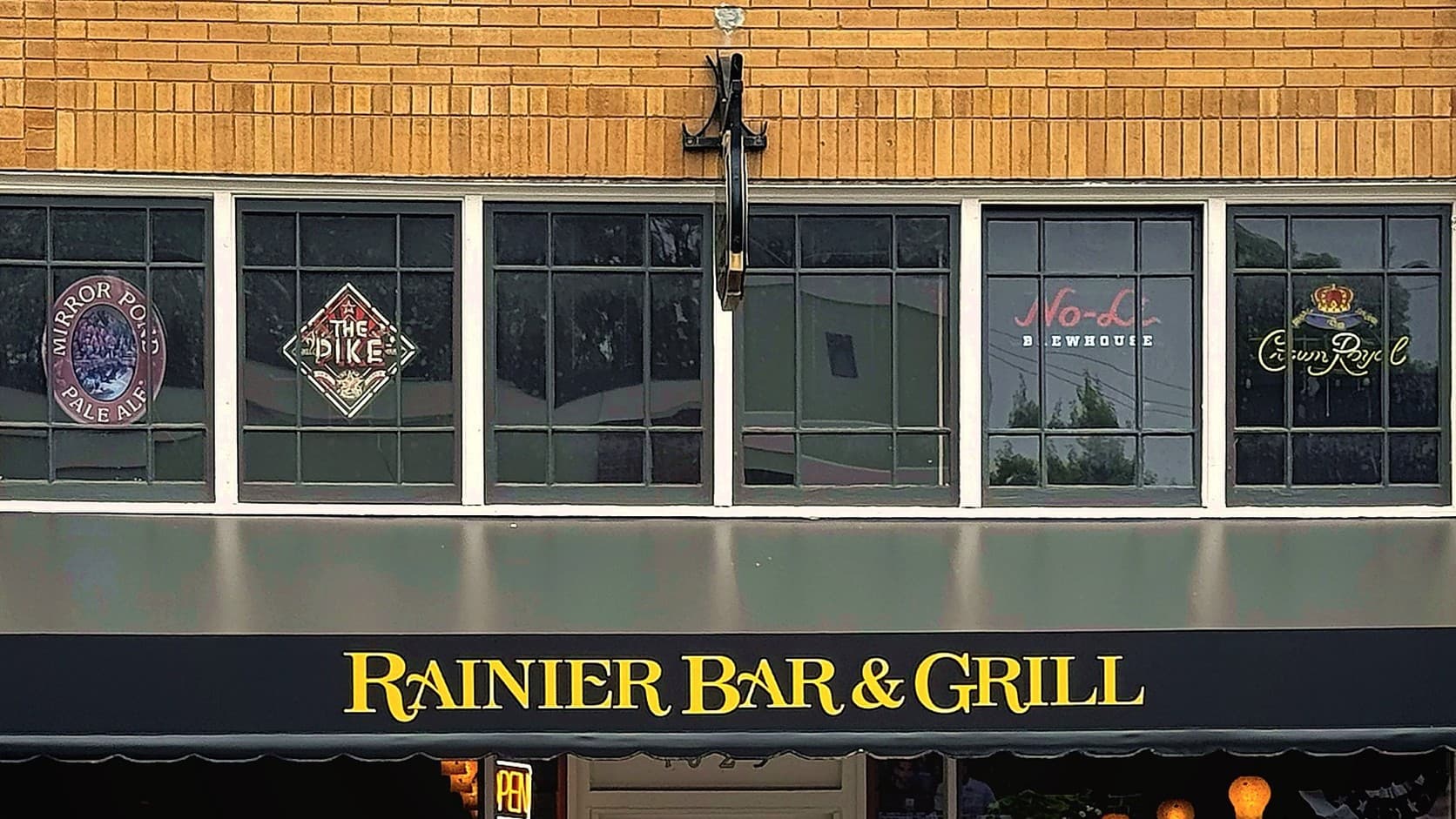 The yellow brick front of Rainier Bar & Grill on Cole Street in Enumclaw: beer and whisky signs in a row of high windows, the restaurant's name in yellow letters on a black awning and the top of the doorway below.