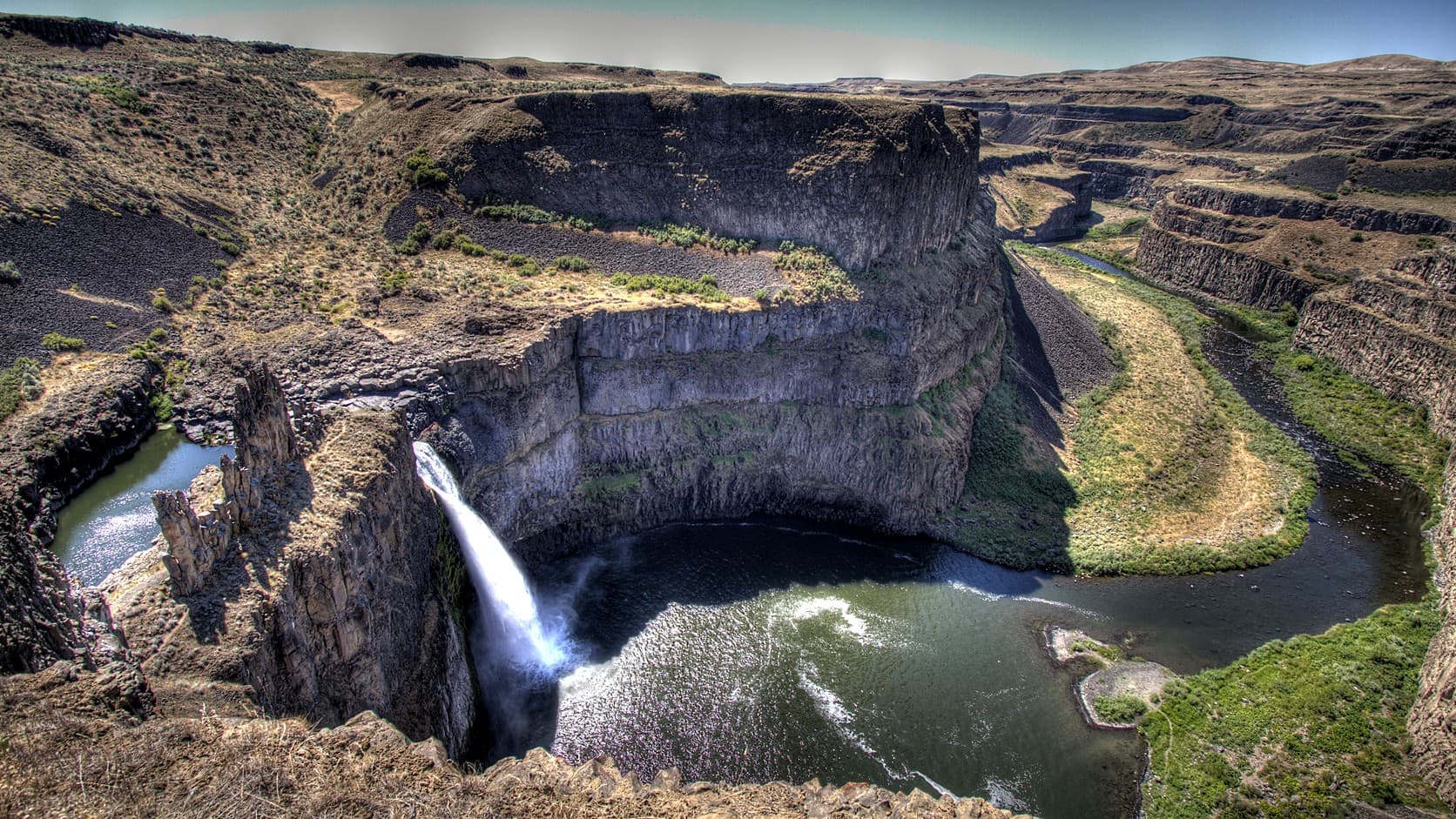 Palouse Falls dropping into its basalt canyon in eastern Washington on a clear day in July 2010, seen from a high overlook with the river winding away downstream